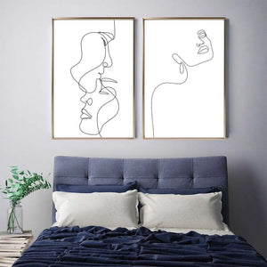 Two black and white single line lady face wall art prints above blue bed