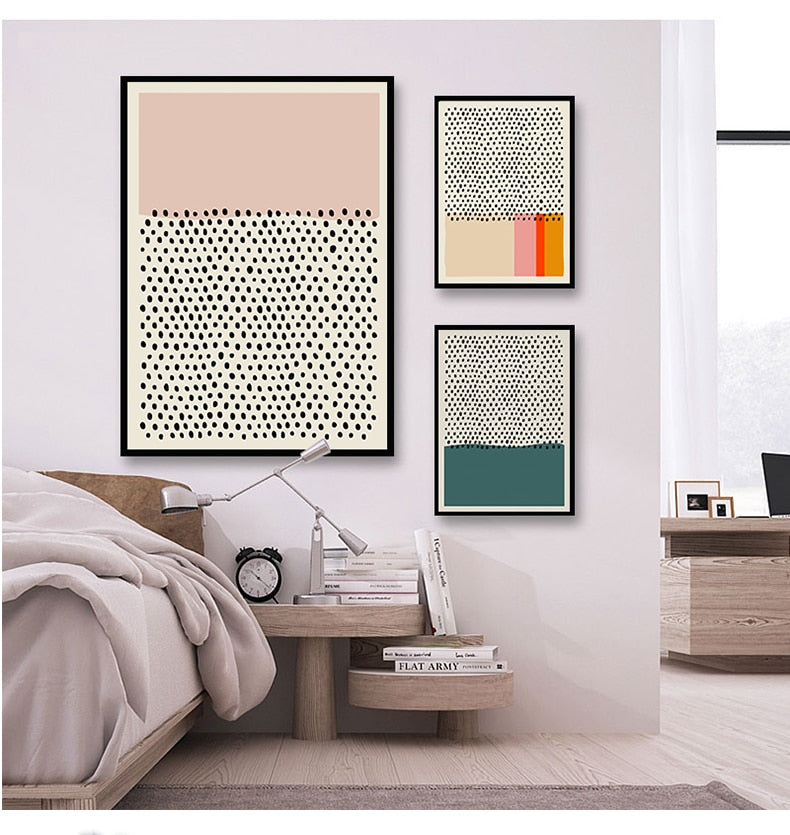 Three minimalist multicoloured wall art prints hanging by a bed
