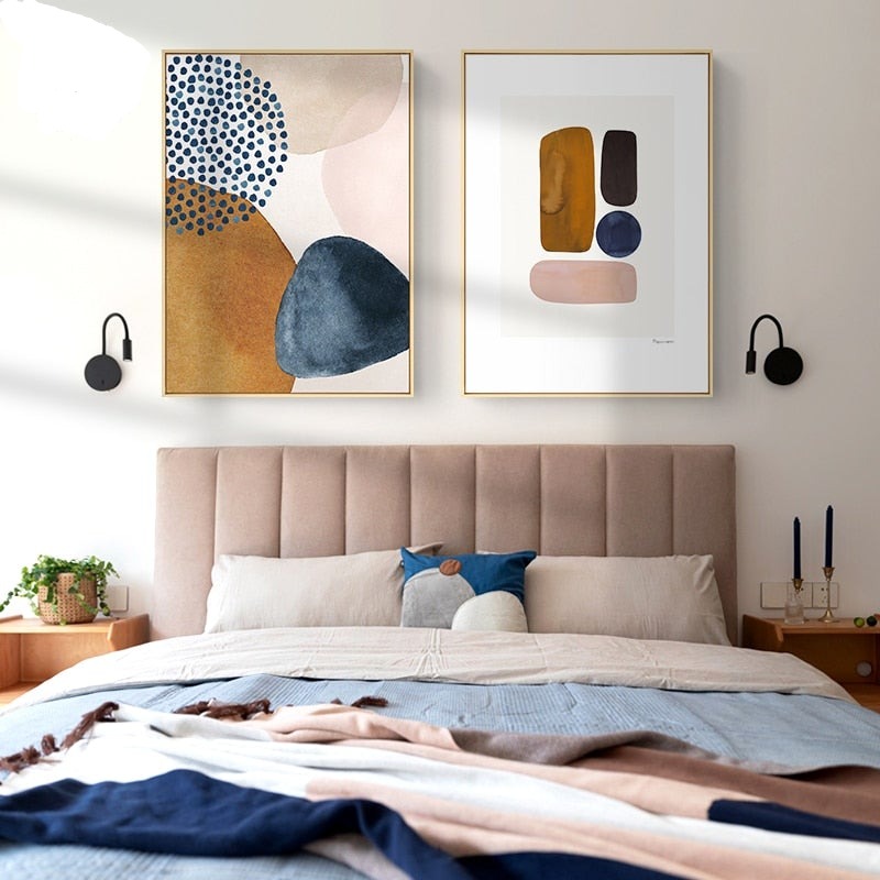Two contemporary blue orange and pink wall art prints hanging above a bed
